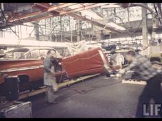 two men working on an old car in a factory