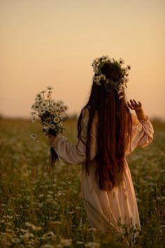 a woman standing in a field with flowers on her head and looking at the sky