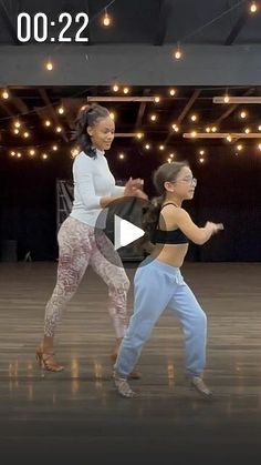 two women are dancing in a dance studio with lights on the ceiling and one woman is wearing