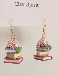 a pair of books with flowers on them are hanging from earwires in front of a sign that says clay quisit