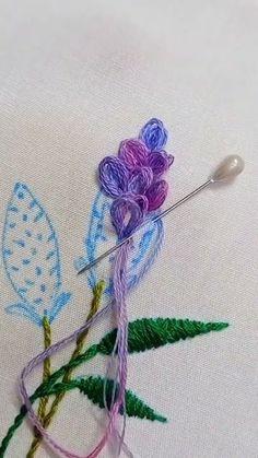 a close up of a needle and thread on a piece of cloth with flowers in the background