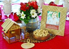 a table topped with pictures and flowers next to a vase filled with white flowers on top of a red cloth covered table