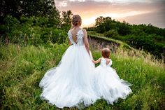 a mother and her daughter are walking through the grass together in their wedding gowns