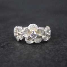 This beautiful flower ring is sterling silver with a cubic zircoia stone. The face of this ring measures 3/8 of an inch north to south. Size: 7 Marks: Peru, 925 Condition: Excellent Sterling Silver Flower Diamond Ring For Wedding, Silver Flower Ring With Cubic Zirconia, Silver Cubic Zirconia Flower Ring, Silver Flower Shaped Cubic Zirconia Ring, Silver Flower-shaped Diamond Ring With Accents, Sterling Silver Brilliant Cut Flower Ring For Anniversary, Silver Flower Shaped Diamond Ring With Accents, Silver Flower Diamond Ring With Accents, Silver Diamond Ring With Flower Shape And Accents