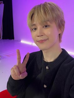 a young man making the peace sign in front of a purple light with his fingers up