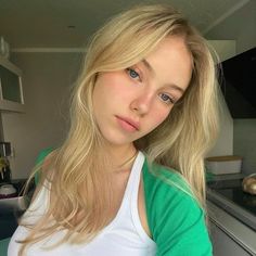 a woman with blonde hair and blue eyes is posing for a photo in the kitchen