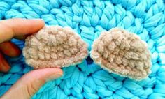 someone is holding two pieces of crocheted wool in their hand, on top of a blue blanket