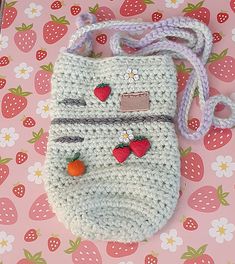 a crocheted purse with strawberries on the front and side, sitting on a pink surface