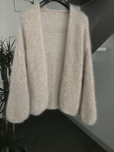 a white sweater hanging on a hanger next to a potted plant in a room