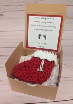 an open box with a crocheted boot in it on a wooden table next to a card