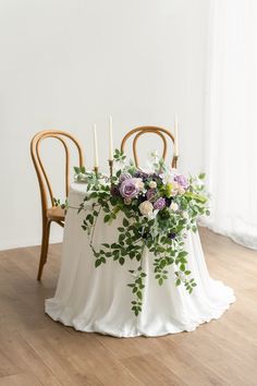 an arrangement of flowers and greenery on a white table cloth with chairs in the background