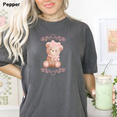 Step into the charming world of yesteryears with our Comfort Colors® Coquette Bear and Bow Shirt, where the timeless essence of the coquette aesthetic meets the soft girl era. This enchanting Teddy Bear Tee embraces femininity with delicate ribbons adorning its design, perfect for the girlie girl with a love for vintage charm. Crafted with premium materials, this Social Club Tee ensures both style and comfort, making it an ideal choice for book clubs, studying, casual outings or cozy evenings. E Cute Cotton T-shirt With Bear Design, Cute Bear Print Crew Neck T-shirt, Cute Bear Print Short Sleeve Tops, Cute Bear Print Top With Short Sleeves, Cute Short Sleeve Tops With Bear Print, Cute Short Sleeve Top With Bear Print, Aesthetic Soft Girl, Soft Girl Era, Shirt Coquette