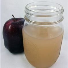 an apple sitting next to a glass jar filled with liquid on top of a white surface