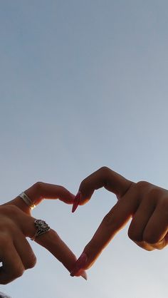 two hands making a heart shape with their fingers in the air against a blue sky