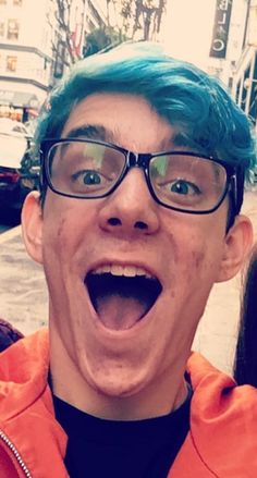 a man with blue hair and glasses making a funny face while standing in the street