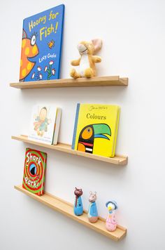 three wooden shelves with books and toys on them against a white wall in a children's room