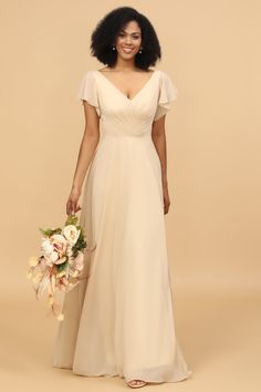 a woman in a white dress holding a bouquet and smiling at the camera while standing against a beige background