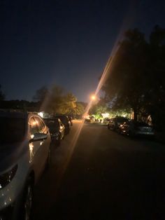 cars parked in a parking lot at night with street lights shining on the buildings and trees