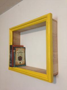 a yellow frame is hanging on the wall next to a bookshelf with a book in it