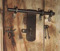 an assortment of keys are hanging on a wooden door with metal handles and latches