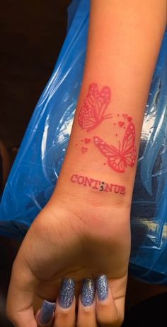 a woman's hand with a butterfly tattoo on her left wrist and the word continus written in red ink