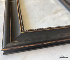 an old black frame with gold trim on the edges and bottom is sitting on a white surface