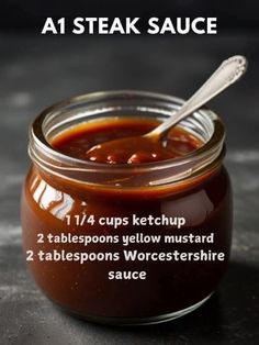 a glass jar filled with ketchup on top of a black table next to a spoon