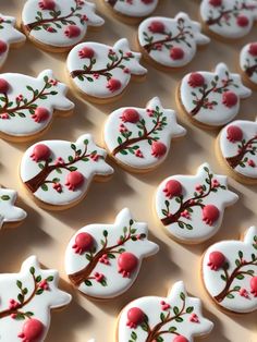 decorated cookies with red flowers and leaves are arranged on a white tablecloth that is laid out in rows