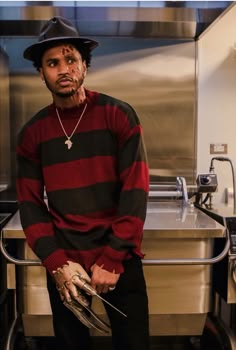 a man in a black hat and red striped shirt standing next to a kitchen sink