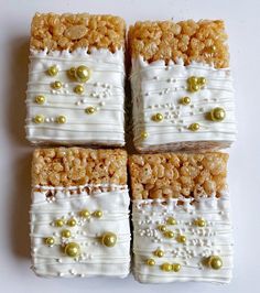 four square pieces of cake with white frosting and gold beads on them, sitting on a table