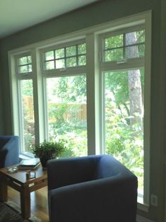 a living room with two blue chairs and a coffee table in front of large windows