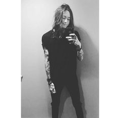 a man with long hair and tattoos is looking at his cell phone while standing in front of a wall