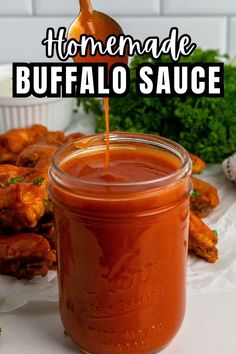 homemade buffalo sauce is being poured into a mason jar with chicken wings in the background