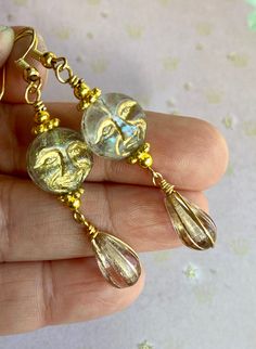 These Czech glass moons are transparent with a gold wash that highlights their features. The moons have a luster finish, which makes them shiny and a little iridescent. I chose Czech glass melon teardrops in clear and gold to pair with the moons. I wrapped the teardrops in gold colored wire and added gold accent beads to tie it all together. The hooks are 18k gold plated. Great whimsical earrings for a fun evening out or for the free spirit on your gift list. All of my earrings come on a hand st Mystical Gold Earrings With Sun And Moon Design, Unique Gold Moon Phase Earrings, Unique Gold Glass Earrings, Mystical Gold Round Earrings, Unique Moon-shaped Gold Earrings, Gold Glass Earrings For Pierced Ears, Unique Gold Moon Earrings, Gold Round Earrings With Sun And Moon Design, Czech Beads Jewelry