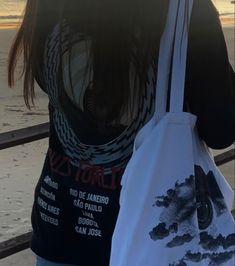 the back of a woman carrying two shopping bags on her shoulder and looking out at the ocean