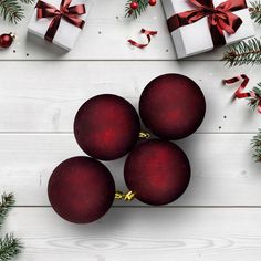 three red christmas baubles on a white wooden table with presents and pine branches