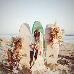 a bride and groom kissing on the beach next to surfboards with floral arrangements around them