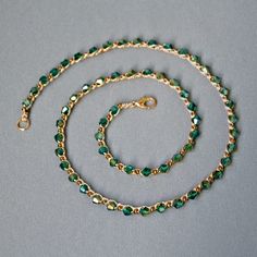 a green and gold beaded necklace on a gray surface with a golden chain attached to it