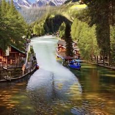 two boats floating on top of a river surrounded by trees and mountains in the background