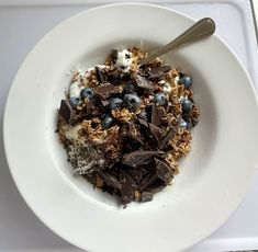 a white bowl filled with cereal and blueberries sitting on top of a counter next to a spoon