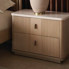 a white vase sitting on top of a wooden cabinet next to a night stand and bed