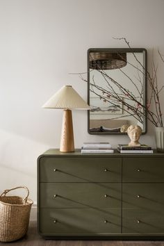 a green dresser with a lamp on top and a mirror above it in a white room