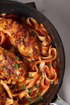 a skillet filled with chicken and pasta covered in sauce, garnished with parsley