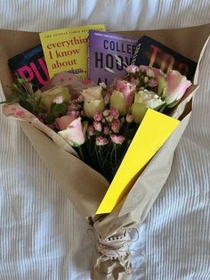 a bouquet of flowers is wrapped in brown paper and sits on a bed with white sheets