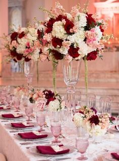 there are many tall vases filled with flowers on the long table set for an event