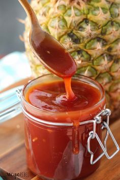 a spoon full of ketchup sitting on top of a wooden table next to a pineapple