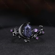 an unusual ring with purple stones and leaves on the outside, sitting on top of a black surface