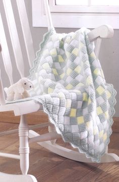 a white rocking chair with a knitted blanket on it and a teddy bear sitting in the rocking chair