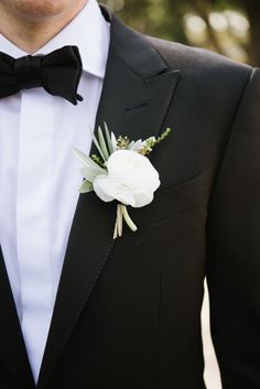 a man wearing a black tuxedo with white flowers on it's lapel