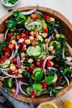 a wooden bowl filled with vegetables and chickpeas on top of a white table